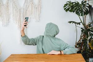 A man without a face takes a selfie of himself. Unrecognizable identity, hacker hiding from the camera, a green sweatshirt, a phone in his hand to hold. photo