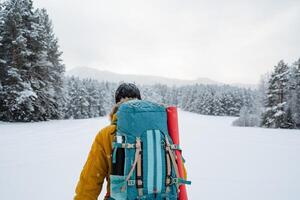 close shot of hiking backpack on the back of the traveler. Snowy forest and rocks. Climbing the mountain in winter. Survival in the wild. photo