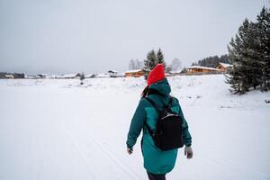 A woman in a green jacket and red hat walking on snow photo