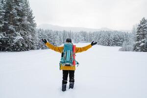 a merry traveler walks with hiking backpack on the back of the traveler. Snowy forest and rocks. Climbing the mountain in winter. Survival in the wild. photo
