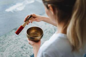 The girl meditates to the sounds of a Tibetan bowl. Bronze singing bowl for Zen relaxation meditation. The hand holds a wooden stick, a blow to the metal extracts a sound. photo