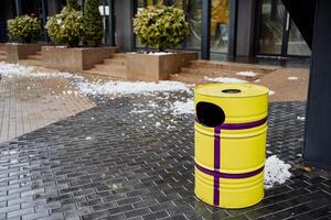 A yellow trash can sitting on a sidewalk photo