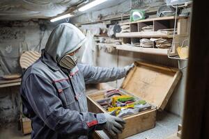Joiner and his woodworking tools. Work in the workshop. Creation of household items from wood. Special clothes and gas mask at the carpenr photo