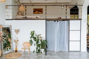 Interior shot. Bright room of the studio. Two-storey room. On the first floor there is a mirror, a chair and pots with flowers, on the second floor there is a room with a bed and a picture. photo