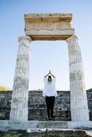 The girl stands between the ancient columns in a yoga pose. Ancient historical construction. Local attractions, entertainment for tourists photo