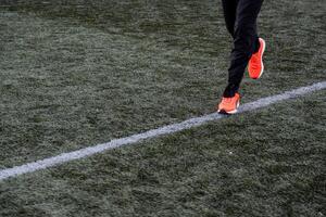 A close shot of a man running across the football field. Bright sports form, good physical training. Playing football, running around the field at the stadium, active sports, training. photo