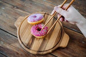 Two donuts with chopsticks on a wooden cutting board photo