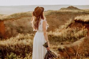 A woman in a white dress and hat stands in the middle of a field photo