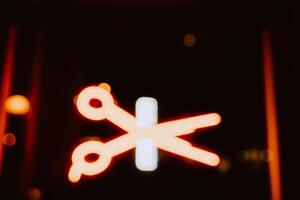 Neon advertising in the form of scissors and combs. Blurry photo. photo