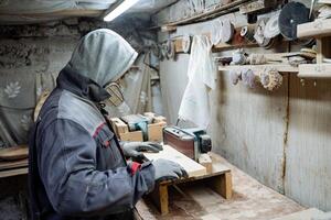 Crafting. A joiner polishes the board. The process of processing boards in the carpentry workshop. Racks with tools, preparatory processes. photo