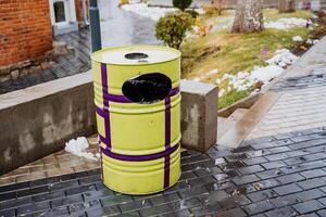 Yellow garbage can on the background of the city. The concept of cleaning and ecology. Round barrel for garbage collection photo