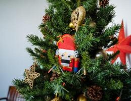 A toy nutcracker hangs on a holiday tree. Festive mood before the New Year and Christmas. Christmas decorations. Christmas balls of gold color and a star on the Christmas tree. photo