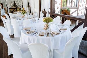 Serving a festive table, placing plates on the table, a Banquet table with a white tablecloth, preparing the dining table for the holiday, Cutlery is arranged according to etiquette. flowers on photo