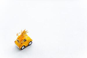 A small yellow car carries yellowed leaves. Autumn minimalistic composition with a toy car on a white background. photo
