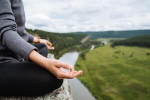 a girl is sitting on a rock in meditation, hands are seen in close-up, a woman's hand is collected in chin mudra, an element of outdoor meditation. Breathing practices. photo