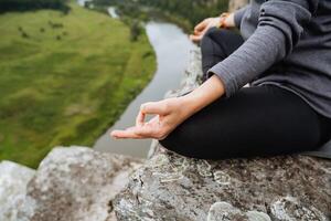 a girl is sitting on a rock in meditation, hands are seen in close-up, a woman's hand is collected in chin mudra, an element of outdoor meditation. Breathing practices. photo
