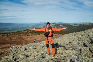 Conquer the mountains in an orange suit arms outstretched, a sense of freedom and wind, a young guy climbed to the top of the mountain and rejoices photo