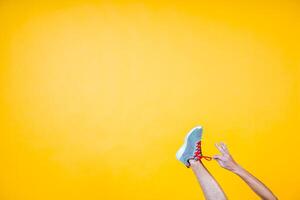foot in a sneaker on a yellow background, hand unties the laces photo