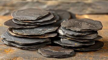 A close-up shot of a stack of smooth black slate coasters on a rustic wooden surface. photo