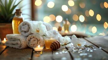 Spa setting with rolled towels, orchids, honey, candles, and oil bottles on a wooden table. photo