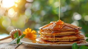 Golden honey drizzling over a stack of fluffy pancakes, set on a rustic wooden table with a blooming flower. photo