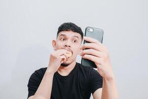 an asian man is enjoying his hamburger while holding his smartphone photo
