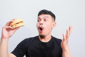 portrait of a young asian man is eating hamburger, isolated on white background. Fast food advertising photo