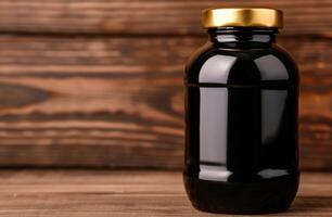 Glossy black glass jar with golden lid on wooden table photo