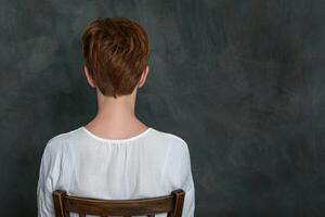 back view of person with short brown hair sitting on a chair photo