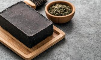 Handmade black soap bar on wooden tray with dried herbs photo
