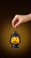 Halloween pumpkin lamp in hand. Halloween autumn concept. On black background vertical banner poster photo