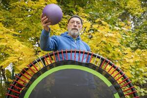 senior man with a medicine ball and a mini trampoline for fitness exercising and rebounding, fall backyard scenery photo