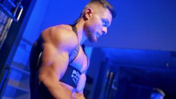 Athletic man with barbell. Muscular sportsman training his arm biceps in the gym on blue light background. Side view. video