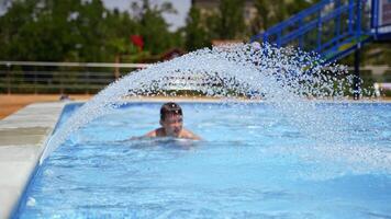 Active boy enjoys in the swimming pool. Happy child having fun near small waterfall inside the pool outdoors. Happy summertime. video