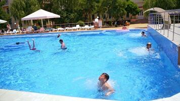 Children in the open swimming pool. Teenage boy jumping into the blue water of the pool in summer time. Happy vacation in water. video