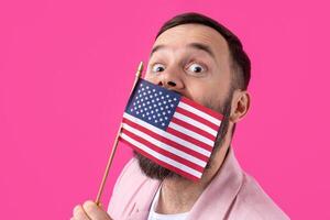 Portrait of a satisfied young man with a beard with an American flag on a red studio background. Great US patriot and defender of freedom. photo