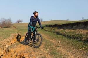 Cyclist in shorts and jersey on a modern carbon hardtail bike with an air suspension fork standing on a cliff against the background of fresh green spring forest photo
