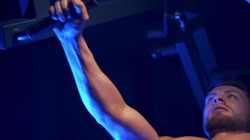 Bodybuilder doing workout in the gym. Strong man with naked torso training his muscles on a simulator. Close-up. Blue filter. video