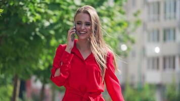 Happy woman talking on the cellphone. Attractive smiling young lady in red dress walking in the city and talks on the mobile phone. Slow motion. video