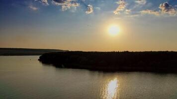 Beautiful evening view on the river at sunset. Golden path in the water from the setting sun on the natural landscape background. Aerial view. Motion camera back. video
