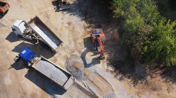 View from above on excavator and two trucks. Excavator working near the machinery with granite stones. Aerial view. video