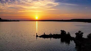View from a drone on the river in the evening. People stand on long stones situated in water at sunset. Camera moves forward. video