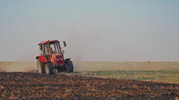 Red tractor at work. Agricultural machine plowing the field at daytime. Cultivation of land outdoors. video