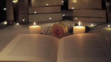 The soft glow of candles illuminates an open book surrounded by a delicate rose and twinkling lights, creating a serene atmosphere perfect for reading at night. video