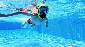 Underwater view of a child diving with mask in the pool. Young boy with mask on face swims in transparent water of a swimming pool. video