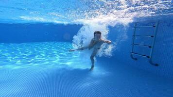 Boy jumping and swimming underwater in the pool. Transparent water background inside the swimming pool and healthy boy swims. video