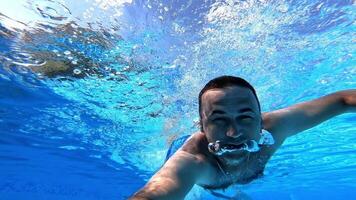 Swimmer swims forward while looking at camera underwater. Man swimming in clear water with underwater camera inside the swimming pool. Summer vacation. video