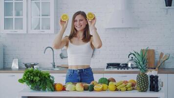 Happy young woman enjoys organic fruit. Beautiful woman with oranges in the kitchen on the background of many fresh vegetables and fruit. video