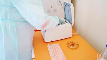 Laboratory assistant near automated device for making analysis. Female worker in protective uniform takes out test tubes from centrifuge in lab. video