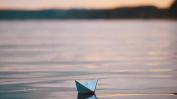 Blue homemade boat on water on blurred evening background. Paper little ship floating alone in calm river at sunset. video